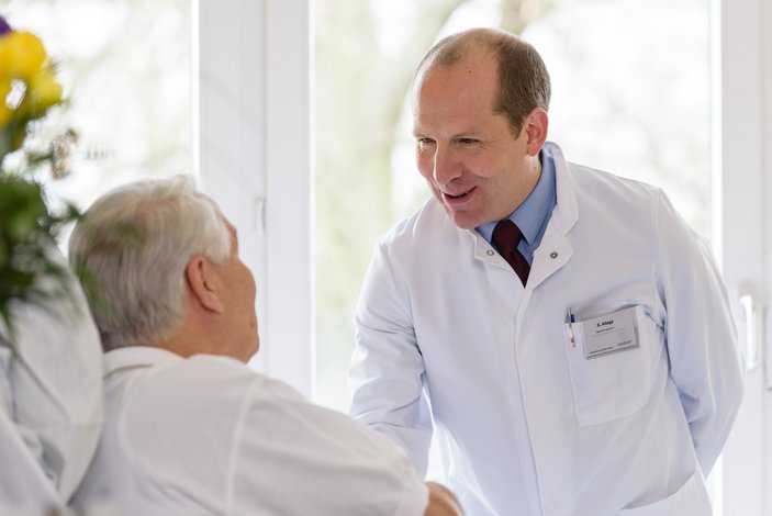 Ein Arzt begrüßt einen Patienten am Krankenbett.