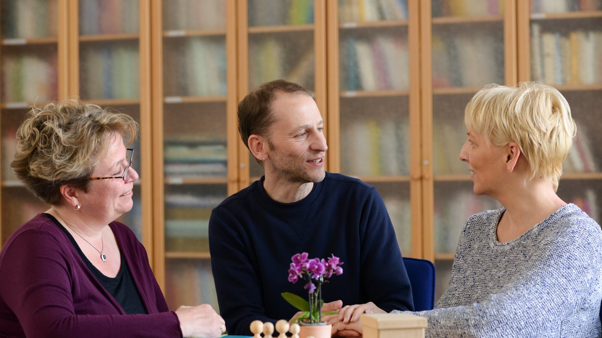 Drei Personen unterhalten sich in einem Beratungsgespräch zum Thema Familienhilfe.