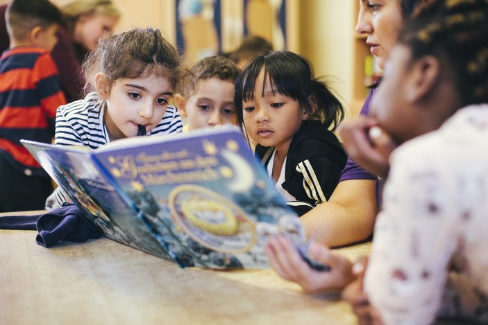 Eine Erzieherin liest Kinder aus einem Buch vor.