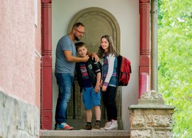 Ein Erzieher begrüßt zwei Kinder an der Haustür.