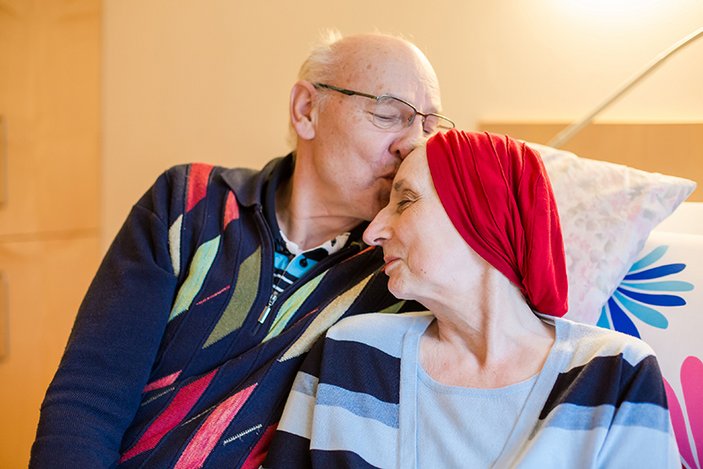 Ein Mann begrüßt seine kranke Frau am Bett im Hospiz.