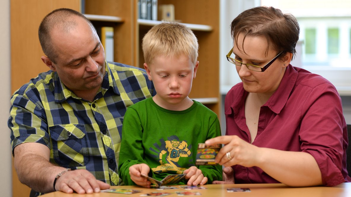 Mutter und Vater spielen mit ihrem Sohn ein Kartenspiel.